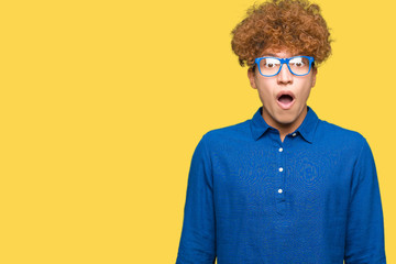 Young handsome man with afro hair wearing blue glasses afraid and shocked with surprise expression, fear and excited face.