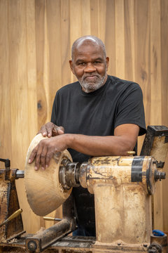 An African American Older Man Creates Works Of Art Through Bowl Turning On A Lathe. This Shows Him Working And Standing By The Machine.