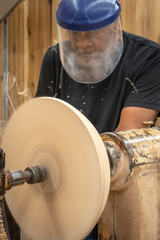 An African American older man creates works of art through bowl turning on a lathe. This shows him working and standing by the machine.