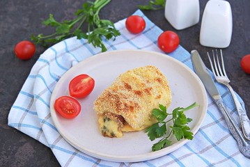 Homemade fillet Cordon Bleu or chicken fillet with ham and cheese on a white clay plate on a dark brown background. Swiss cuisine. Selective focus.
