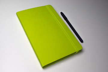 green notebook with a pen lying on a white table inclined