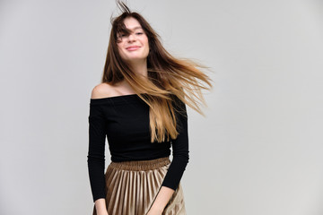 Photo portrait of a beautiful pretty brunette girl in a black sweater on a gray background. A woman is satisfied with her life, she stands in front of the camera, smiling and talking. Made in studio.