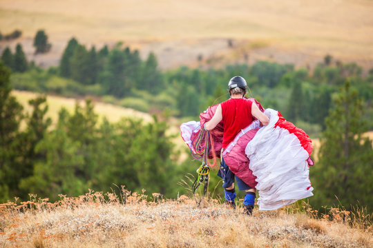 A man carries his kite to a take off area at the top of Paradise Ridge during a father and son paragliding outing.
