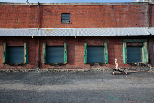 A fit, blonde woman does yoga in front of an old brick warehouse in downtown Spokane, Washington.