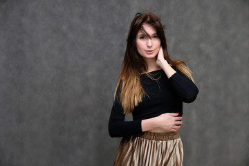 Photo portrait of a beautiful pretty brunette girl in a black sweater on a gray background. A woman is satisfied with her life, she stands in front of the camera, smiling and talking. Made in studio.