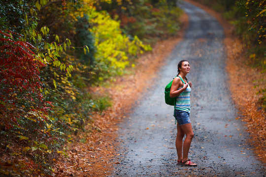 A woman hiking along a colorful bend in Old Nags Head Woods Road on a rainy autumn day. The narrow road is one of only two roads that access the Nags Head Woods Preserve.