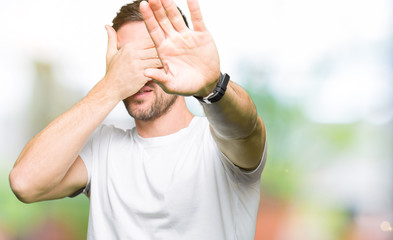 Handsome man wearing casual white t-shirt covering eyes with hands and doing stop gesture with sad and fear expression. Embarrassed and negative concept.