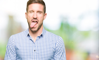 Handsome business man with blue eyes sticking tongue out happy with funny expression. Emotion concept.