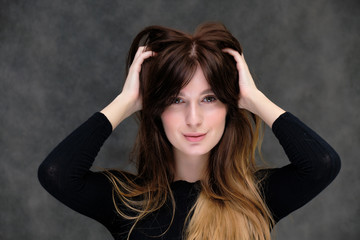 Obraz premium Beauty portrait of a beautiful pretty brunette girl in a black sweater on a dark gray background. A woman is happy with life, she is standing in front of the camera, smiling. Made in a studio.