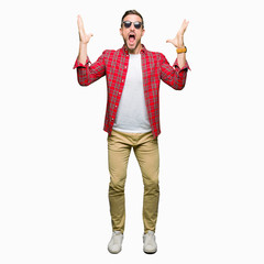 Handsome man wearing fashion sunglasses celebrating crazy and amazed for success with arms raised and open eyes screaming excited. Winner concept