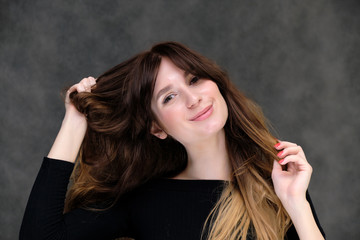 Fototapeta premium Beauty portrait of a beautiful pretty brunette girl in a black sweater on a dark gray background. A woman is happy with life, she is standing in front of the camera, smiling. Made in a studio.