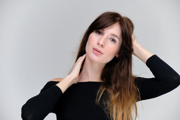 Beauty portrait of a beautiful pretty brunette girl in a black sweater on a light gray background. A woman is happy with life, she is standing in front of the camera, smiling. Made in a studio.