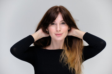 Fototapeta premium Beauty portrait of a beautiful pretty brunette girl in a black sweater on a light gray background. A woman is happy with life, she is standing in front of the camera, smiling. Made in a studio.