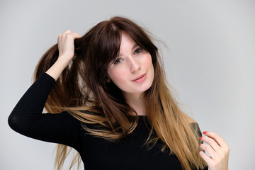 Beauty portrait of a beautiful pretty brunette girl in a black sweater on a light gray background. A woman is happy with life, she is standing in front of the camera, smiling. Made in a studio.