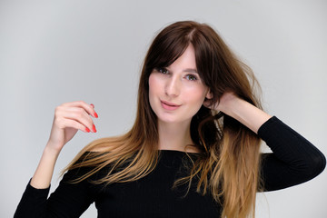 Fototapeta premium Beauty portrait of a beautiful pretty brunette girl in a black sweater on a light gray background. A woman is happy with life, she is standing in front of the camera, smiling. Made in a studio.
