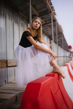 Woman ballerina in the city stands sitting on the railing
