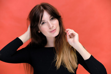 Fototapeta premium Beauty portrait of a beautiful pretty brunette girl in a black sweater on a red background. A woman is happy with life, she is standing in front of the camera, smiling. Made in a studio.