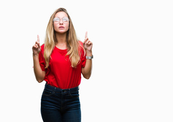 Obraz na płótnie Canvas Young beautiful blonde woman wearing glasses over isolated background amazed and surprised looking up and pointing with fingers and raised arms.