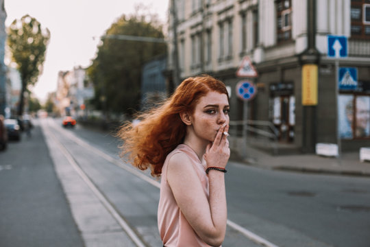 Young woman smoking while crossing road in city