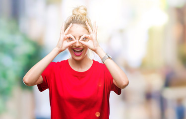 Young beautiful blonde woman wearing red t-shirt and glasses over isolated background doing ok gesture like binoculars sticking tongue out, eyes looking through fingers. Crazy expression.