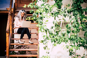 Adult alternative diversity people concept white and grey long hair beautiful woman with laptop computer sitting on a wooden stairs outside home - happy free people with internet technology everywhere