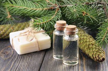 Two bottles of spruce essential oil, natural soap and fir branches behind.