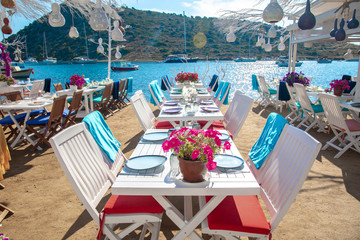 View of restaurant or cafe and bougainvillea flowers on beach in Gumusluk, Bodrum city of Turkey. Aegean seaside style colorful chairs, tables and flowers in Bodrum town near beautiful Aegean Sea.