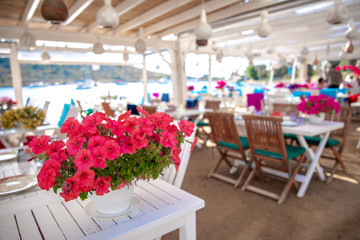View of restaurant or cafe and bougainvillea flowers on beach in Gumusluk, Bodrum city of Turkey. Aegean seaside style colorful chairs, tables and flowers in Bodrum town near beautiful Aegean Sea.