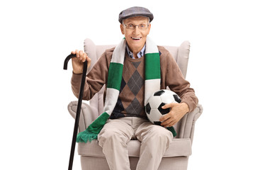 Senior man with a football and a scarf sitting in an armchair