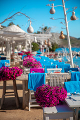 View of restaurant or cafe and bougainvillea flowers on beach in Gumusluk, Bodrum city of Turkey. Aegean seaside style colorful chairs, tables and flowers in Bodrum town near beautiful Aegean Sea.