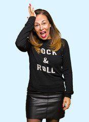 Beautiful middle age woman wearing rock and roll sweater surprised with hand on head for mistake,...