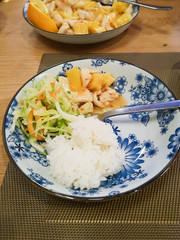 Chinese food on blue and white floral print plates, cabbage and carrot salad, steamed buns, pineapple and orange chicken and steamed rice in a Chinese restaurant