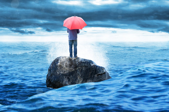 Mann mit Regenschirm steht auf einem Fels im Meer