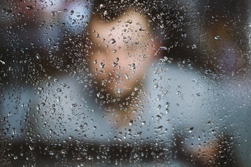 Fototapeta premium Male man ghostly blurred silhouette through the window with raindrops reaching for the glass. A request for help, depression blurred bokeh background. Refusal denial of alcohol and drugs