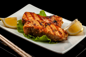 Grilled trout with lemon on a platter on a black table