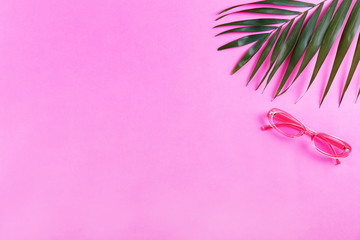 Green palm leaves with accessories and clothing items or summer symbols, beachwear on colored paper textured background with a lot of copy space for text. Top view, flat lay.