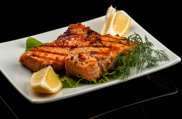 Grilled trout with lemon on a platter on a black table