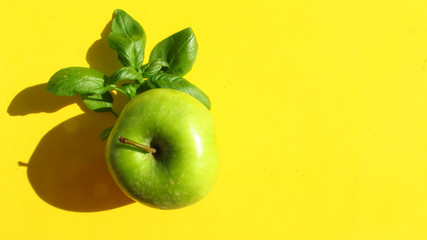 close up green apple and basil leaf on yellow background, top view