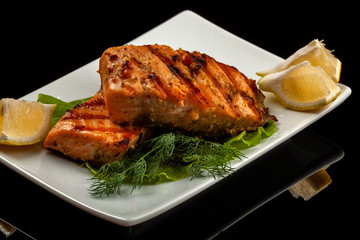 Grilled trout with lemon on a platter on a black table