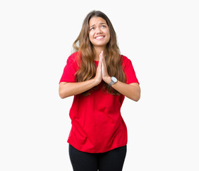 Young beautiful brunette woman wearing red t-shirt over isolated background begging and praying...