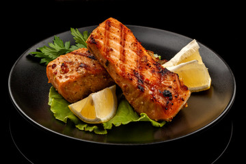 Grilled trout with lemon on a platter on a black table