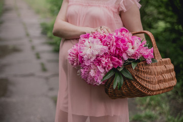 pregnant girl in a pink dress with a pony basket hold her hand on her stomach on a summer day in the park
