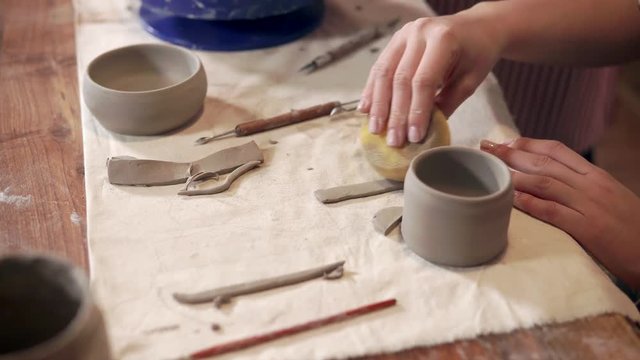 Woman is processing clay detail in workshop, close-up view of hands and table