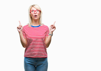 Young beautiful blonde woman wearing glasses over isolated background amazed and surprised looking up and pointing with fingers and raised arms.