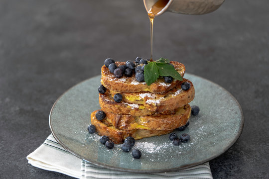 Stack of french toast with blueberries and pouring maple syrup