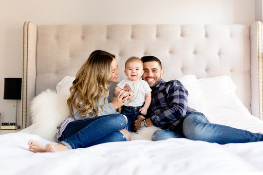 Mom and dad smiling with cute baby boy on bed in bedroom