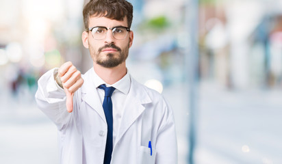 Young professional scientist man wearing white coat over isolated background looking unhappy and angry showing rejection and negative with thumbs down gesture. Bad expression.