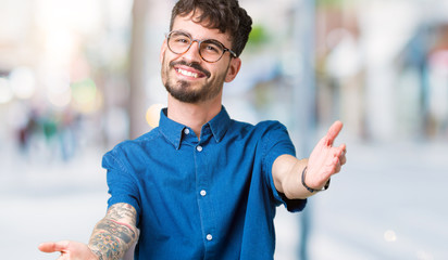 Young handsome man wearing glasses over isolated background looking at the camera smiling with open arms for hug. Cheerful expression embracing happiness.