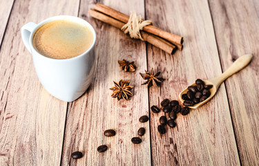 Cup of hot coffee, cinnamon sticks and coffee beans spilling out from a wooden scoop on wooden rustic table. Close-up.