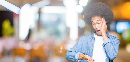 Young african american man with afro hair Looking at the watch time worried, afraid of getting late